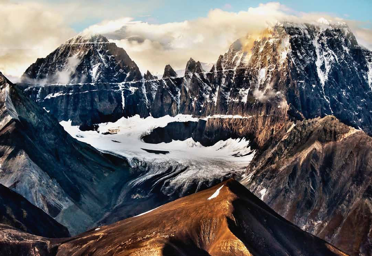 full-screen-slider-bg2 This formation—mountain peaks forming a circle or semi-circle—is called a
“cirque,” which is a French term derived from Latin for “circle.”
This particular glacier is visible only from the air; it was photographed during a
short flight from Copper Center to McCarthy, Alaska, just before sunset.
You can plainly see that this glacier, which at one time extended well up the sides
of the cirque, is diminishing. You can see the terminal moraine, lower left, and how
rapidly the glacier is retreating from it (leaving a new moraine as it withdraws).